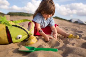 4-6 jähriges Mädchen mit roter Hose, Froschrucksack und Buddelförmchen beim Sandspielen am Strand 4-6 jähriges Mädchen mit roter Hose, Froschrucksack und Buddelförmchen beim Sandspielen am Strand