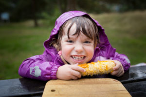 4-6 years old girl in wet purple rain jacket eating a corncob 4-6 years old girl in wet purple rain jacket eating a corncob
