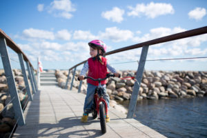 4-6 jähriges Mädchen fährt auf rotem Kinderfahrrad auf einer Brücke an der Ostseeküste 4-6 jähriges Mädchen fährt auf rotem Kinderfahrrad auf einer Brücke an der Ostseeküste