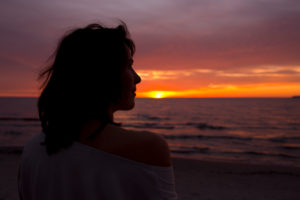 30-40 jährige Frau betrachtet Sonnenaufgang in kräftigen orangenen Farben an der Ostsee 30-40 jährige Frau betrachtet Sonnenaufgang in kräftigen orangenen Farben an der Ostsee
