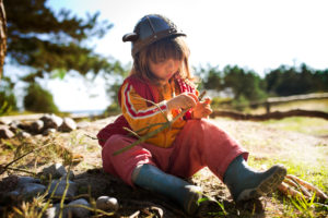 4-6 jähriges Mädchen mit Wikingerhelm und roter Latzhose im Sand am Waldrand 4-6 jähriges Mädchen mit Wikingerhelm und roter Latzhose im Sand am Waldrand