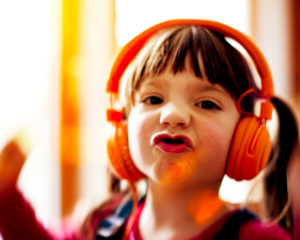 4-6 jähriges Kind tanzt mit orangenen Kopfhörern, Mimik, Porträt 4-6 jähriges Kind tanzt mit orangenen Kopfhörern, Mimik, Porträt