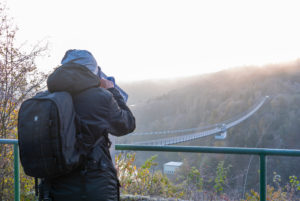 Germany, Saxony-Anhalt, Upper Harz, tourist with backpack, looks through binoculars, suspension bridge at the Rappbodetalsperre, Harz.