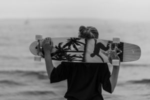 Mädchen mit Longboard steht vor einem Fischerboot Mädchen mit Longboard steht vor einem Fischerboot