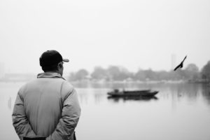 An elderly man staning in front of a lake in China looking into the distance