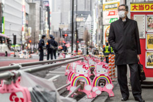 A serious businessman with surgical mask next to a 'Hello Kitty'- road barrier
