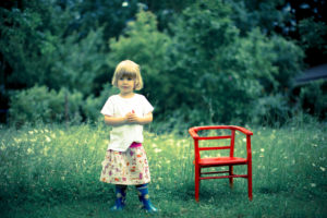 Girl standing in a meadow next to a red child's chair Girl standing in a meadow next to a red child's chair