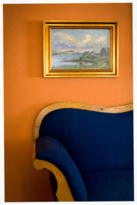 Old dark blue sofa, old oil painting with golden frame, orange-coloured wall Old dark blue sofa, old oil painting with golden frame, orange-coloured wall