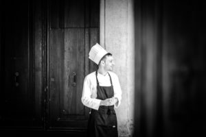 Chef, young man with chef's hat and apron, smiling, door in the background, black and white photo Chef, young man with chef's hat and apron, smiling, door in the background, black and white photo