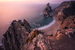 Travel to Praia da Ursa Beach, Sintra, Portugal. Landscape scene in lilac epic sunset light. Sharp cliffs and surreal coasty of Atlantic Ocean. Travel to Praia da Ursa Beach, Sintra, Portugal. Landscape scene in lilac epic sunset light. Sharp cliffs and surreal coasty of Atlantic Ocean.