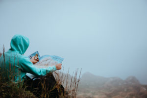 Traveler with a map sitting on the hill of a mountain in front of a gorgeous panorama view to the valley. Traveler with a map sitting on the hill of a mountain in front of a gorgeous panorama view to the valley.