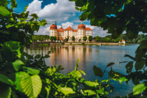 Castle Moritzburg in Saxony near Dresden. Framed by spring lush foliage leaves in foreground with reflection in pond Springtime. Germany. Castle Moritzburg in Saxony near Dresden. Framed by spring lush foliage leaves in foreground with reflection in pond Springtime. Germany.