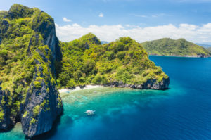 Aerial drone view of tropical beach with lonely boat on Entalula Island. Karst limestone formation mountain surrounded by blue ocean and beautiful coral reef. Aerial drone view of tropical beach with lonely boat on Entalula Island. Karst limestone formation mountain surrounded by blue ocean and beautiful coral reef.