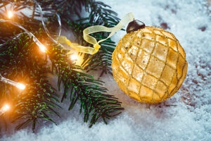 Golden Christmas ball on snow near branches of fir tree. Festive background with copy space.