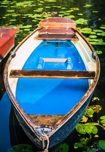 Blue colored wooden rowboat at the pier of a lake for rent surrounded by nenuphar. Municipal city park. Hamburg.