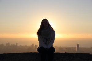 Junge Frau sitzt auf einer Mauer. Hinter ihr geht die Sonne über dem Meer und Barcelona auf. Junge Frau sitzt auf einer Mauer. Hinter ihr geht die Sonne über dem Meer und Barcelona auf.