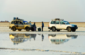 Two four-wheel drive vehicles with attendant staff stand in front of a brine on the edge of the Assale salt lake, Hamedala, Danakil Valley, Afar Region, Ethiopia Two four-wheel drive vehicles with attendant staff stand in front of a brine on the edge of the Assale salt lake, Hamedala, Danakil Valley, Afar Region, Ethiopia