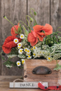 Flower arrangement made of poppy blossoms, camomile and other field flowers in an old wooden box with grasp, sign with the writing "DANKE" Flower arrangement made of poppy blossoms, camomile and other field flowers in an old wooden box with grasp, sign with the writing "DANKE"