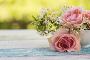 Flower arrangement of pink roses and small white blossoms in a small old white cup on wooden board with green background light, Flower arrangement of pink roses and small white blossoms in a small old white cup on wooden board with green background light,