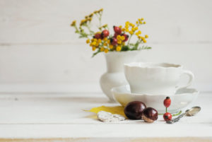 floral autumnal still life with coffee cover and flower vase with yellow blossoms and red rose hips floral autumnal still life with coffee cover and flower vase with yellow blossoms and red rose hips