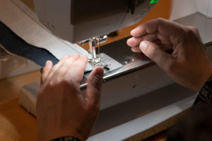Detail shot of woman's hands on sewing machine at sewing workshop with fabric samples Detail shot of woman's hands on sewing machine at sewing workshop with fabric samples