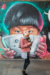 England, London, Southwark, Clink Street, Girl Texting While Walking Past Wall Mural Street Art depicting Asian Child Eating from Bowl England, London, Southwark, Clink Street, Girl Texting While Walking Past Wall Mural Street Art depicting Asian Child Eating from Bowl
