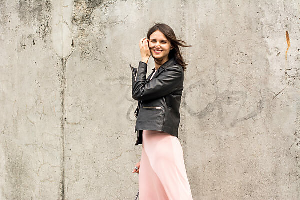 Bildagentur | mauritius images | Portrait of young woman wearing black leather jacket and pink dress in front of concrete wall Bildagentur | mauritius images | Portrait of young woman wearing black leather jacket and pink dress in front of concrete wall