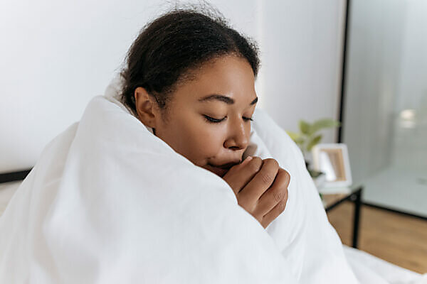 Woman with vitiligo holding pillow between legs on bed in front of white  wall at home