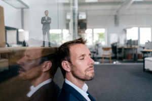 Businessman sitting in his office with his 3D portrait behind a glass pane