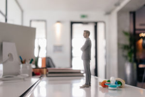 Businessman figurine standing on desk with pacifier and toys