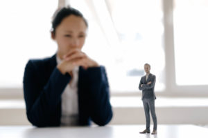 Businesswoman watching businessman figurine, standing on her desk