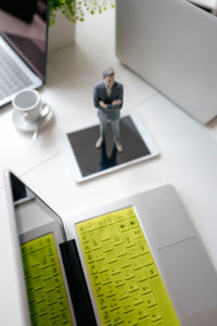 Businessman figurine standing on a desk with mobile devices and a cup of coffee