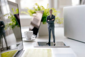 Businessman figurine standing on a desk with mobile devices and a cup of coffee