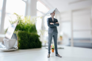 Businessman figurine standing on desk, balancing a laptop on top of his head
