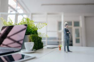 Businessman figurine standing on desk, balancing a cup of coffee on top of his head