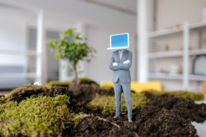 Businessman figurine with laptop head standing on green moss