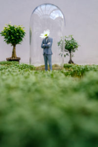 Businessman figurine with flower head standing park under bell jar