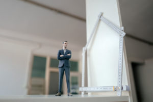 Businessman figurine standing on table with pocket rule, shaping a house
