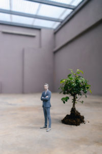 Businessman figurine standing next to a little tree
