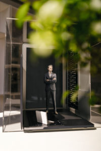 Businessman figurine standing on portable devices under a green plant