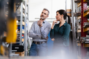 Businessman and businesswoman having a work meeting in storehouse of a factory Businessman and businesswoman having a work meeting in storehouse of a factory