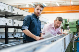Two men examining piece of metal in a factory Two men examining piece of metal in a factory