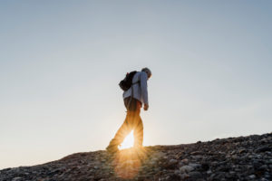 Sunbeam through active senior man hiking on mountain against sky Sunbeam through active senior man hiking on mountain against sky