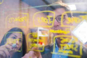 Businessman and woman brainstorming taking notes on glass pane in office Businessman and woman brainstorming taking notes on glass pane in office