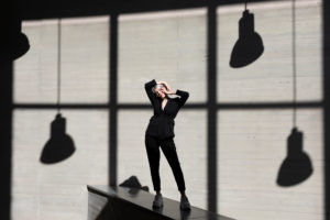 Stylish businesswoman wearing suit standing on retaining wall with sunlight and shadow in background Stylish businesswoman wearing suit standing on retaining wall with sunlight and shadow in background