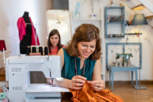 Smiling female tailor looking at fabric by sewing machine in design studio Smiling female tailor looking at fabric by sewing machine in design studio