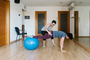 Physiotherapist assisting patient in balancing on fitness ball at health club Physiotherapist assisting patient in balancing on fitness ball at health club