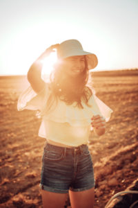 Cheerful young woman standing on field against sky during sunset Cheerful young woman standing on field against sky during sunset