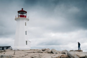 Man standing near Peggys Point Lighthouse on rock formation against cloudy sky, Nova Scotia, Canada Man standing near Peggys Point Lighthouse on rock formation against cloudy sky, Nova Scotia, Canada