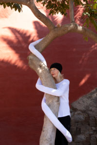 Thoughtful woman with artificial long hands embracing tree trunk against wall Thoughtful woman with artificial long hands embracing tree trunk against wall